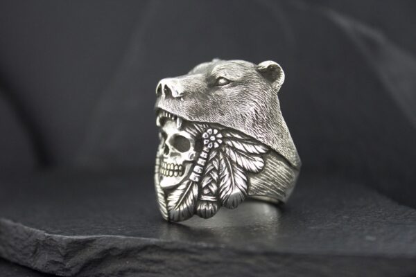 A detailed silver ring featuring a bear head and a skull with wings.