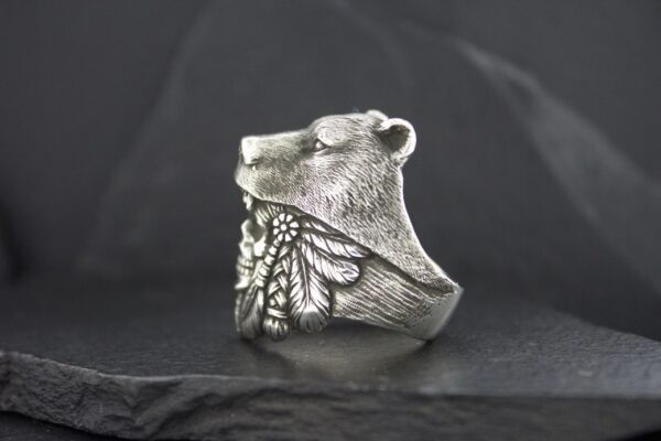 A silver ring featuring a bear head and intricate leaf designs.