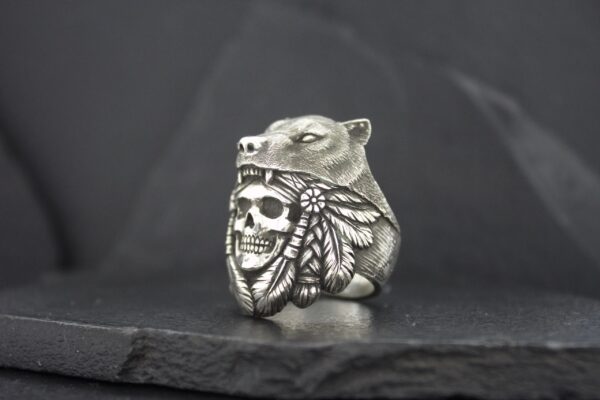 A silver ring featuring a bear holding a skull and a bee.