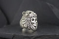 A silver ring featuring a bear and a skull with feathers design.