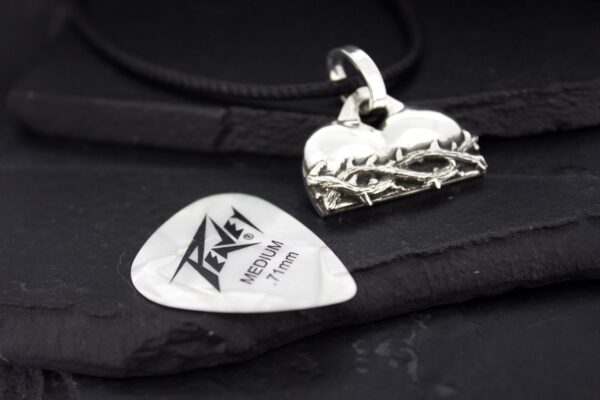 A guitar pick and a metallic pendant on a black surface.