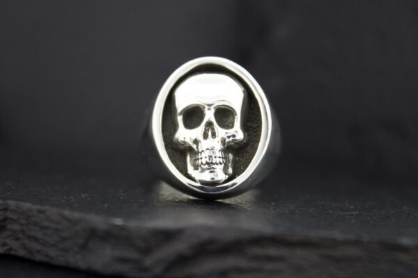 Silver ring with a detailed skull design on a black background.