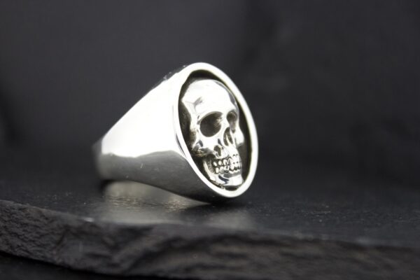 A silver ring featuring a detailed skull engraving on its face.