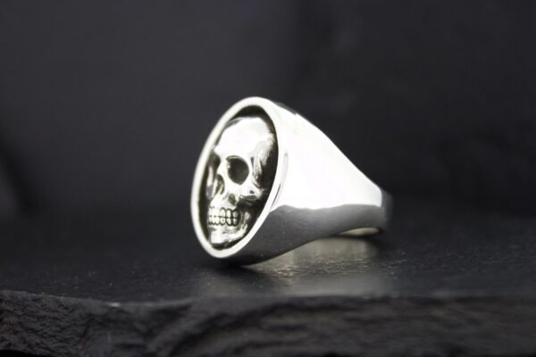 Silver ring featuring a detailed skull face on a black background.