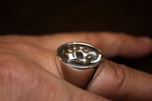 Close-up of a hand holding a silver ring with a reflective, curved surface.