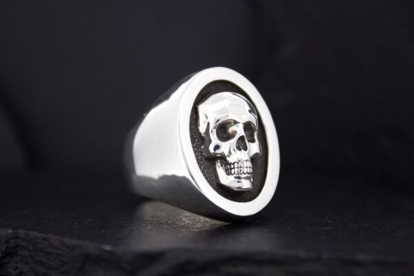 Silver ring with a detailed skull design on a black background.