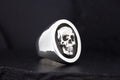 Silver ring with a detailed skull design on a black background.