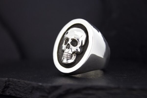 A silver ring with a detailed skull design on a black background.