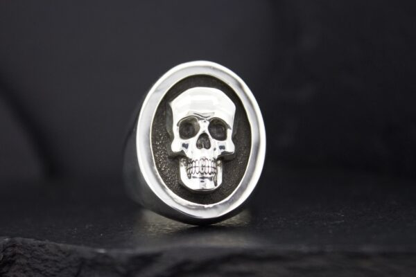 Silver ring featuring a detailed skull design on a black background.