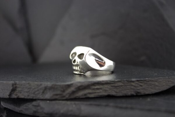 Silver skull-shaped ring on a dark surface.