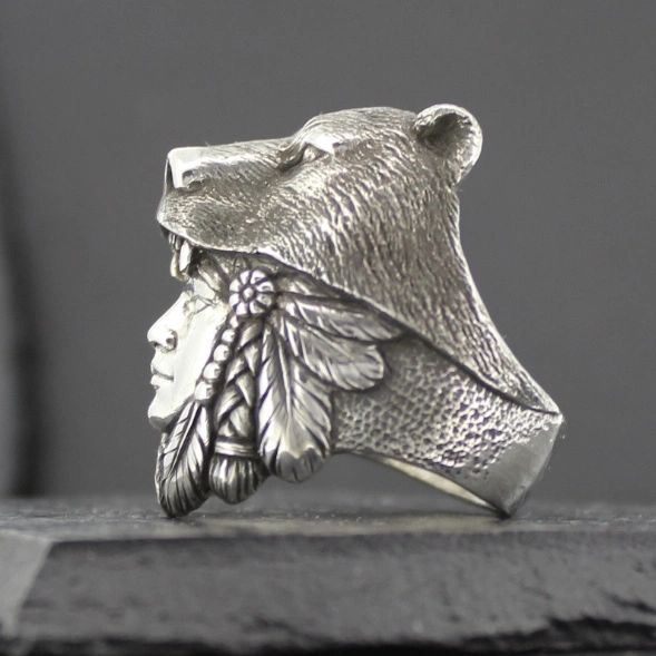 A silver ring featuring a bear head and a Native American profile with feathers.