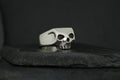Silver skull ring with black eye sockets on a dark surface.