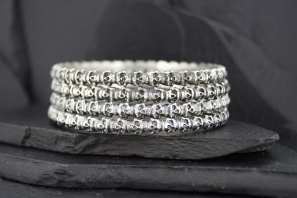 Stacked silver rings with intricate designs on a dark background.