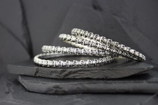 Close-up of silver spiral bangles on a dark textured surface.
