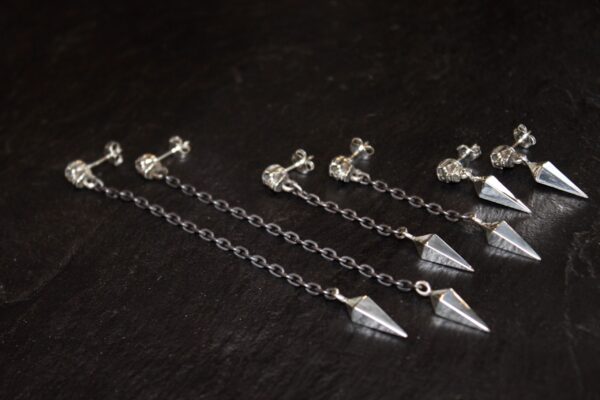 Silver chain earrings with geometric pendants on a dark surface.