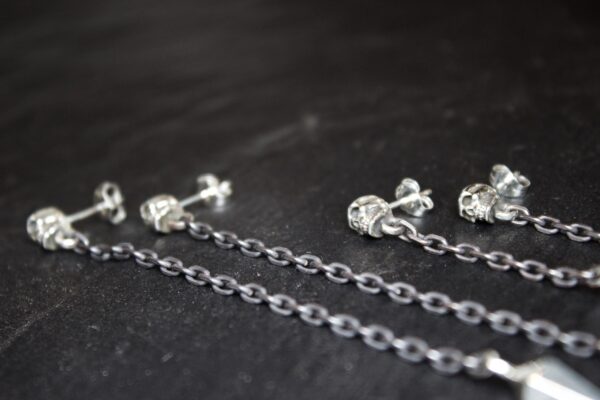 Close-up of silver jewelry chains and earrings on a dark surface.