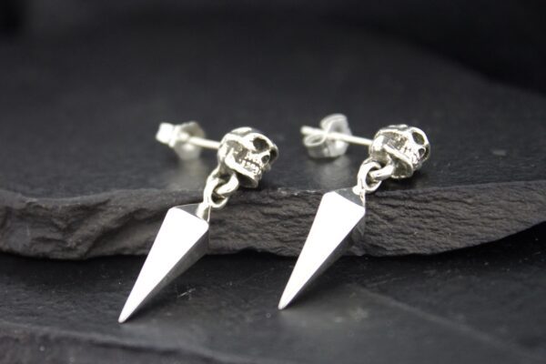 Silver skull and spike stud earrings on a dark background.