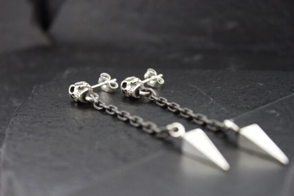 Close-up of silver chain earrings with geometric pendants on a dark surface.