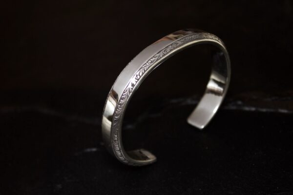 Silver cuff bracelet with intricate engravings on a dark background.