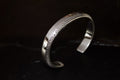 Silver cuff bracelet with intricate engravings on a dark background.