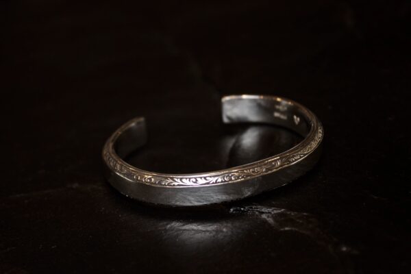 A silver cuff bracelet with intricate engravings on a dark surface.