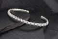 Elegant silver bracelet with intricate skull designs on a dark background.