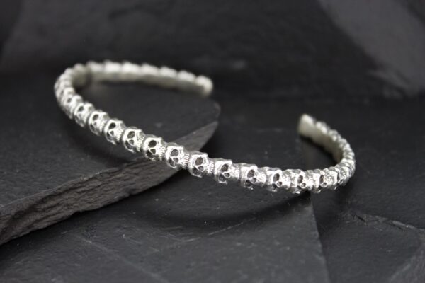 Elegant silver bracelet with intricate skull designs on a dark background.