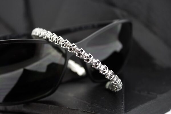 Silver bracelet adorned with small skull charms on a black surface.