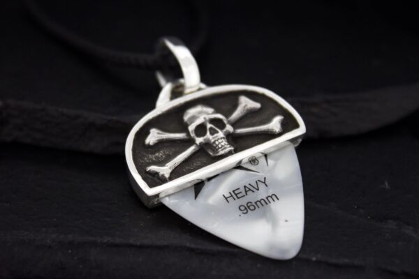 A guitar pick holder with a skull and crossbones design containing a heavy 0.96mm pick.