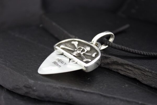 Close-up of a silver guitar pick pendant with an engraved design on a black surface.