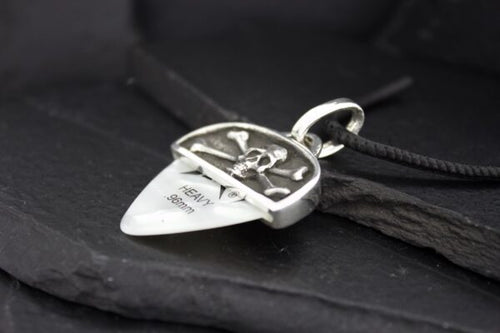 Close-up of a silver guitar pick pendant with an engraved design on a black surface.