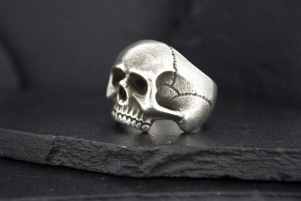A detailed silver skull ring on a dark surface.