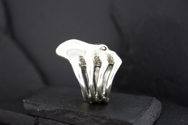 Silver ring shaped like a hand skeleton on a black surface.
