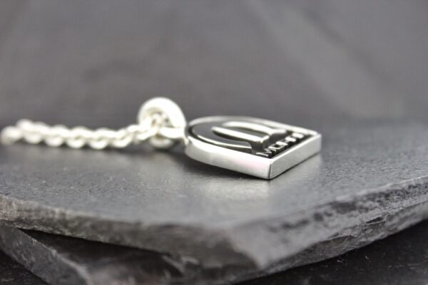 Close-up of a silver pendant on a chain resting on a dark stone surface.