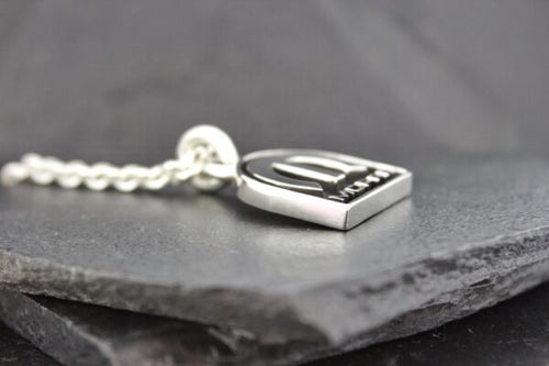 Close-up of a silver pendant on a chain resting on a dark stone surface.