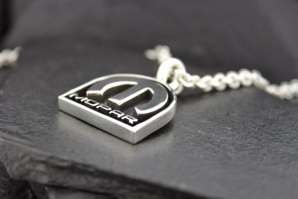 Close-up of a silver pendant with a raised logo on a chain.