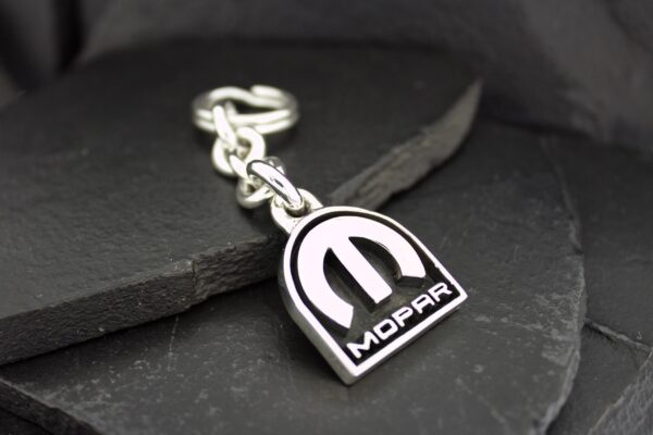 A Mopar keychain with a silver chain on a dark surface.