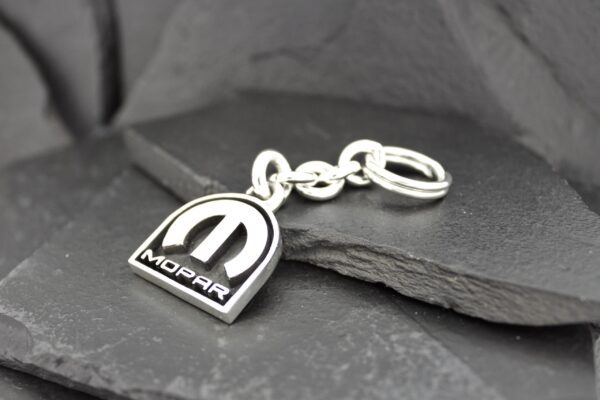 A Mopar keychain with a metallic finish on a stone surface.