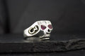 Silver skull ring with red gemstone eyes and a black background.