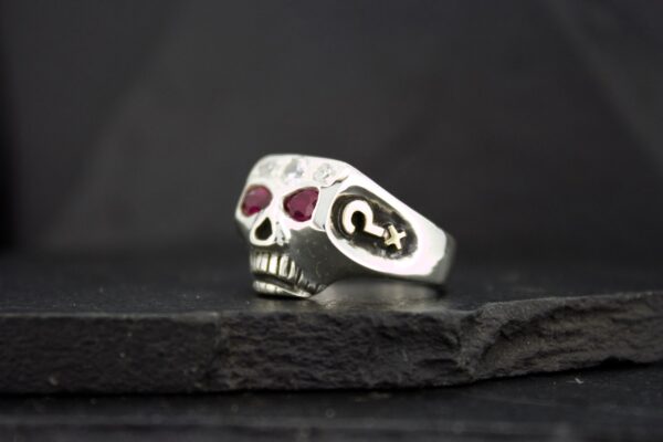 Silver skull ring with red gemstone eyes on a dark surface.