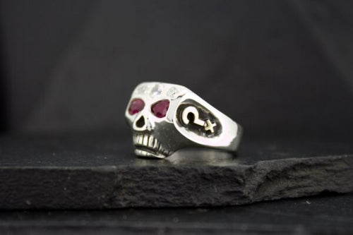 Silver skull ring with red gemstone eyes on a dark surface.