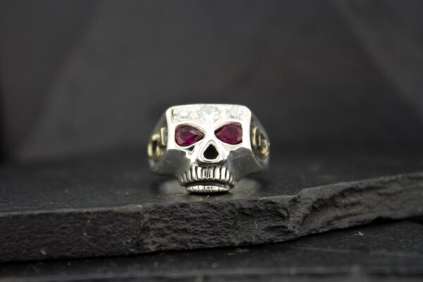 Silver skull ring with red gemstone eyes on dark background.