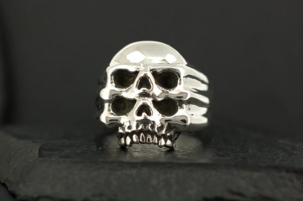 A silver skull-shaped ring with detailed features on a dark background.