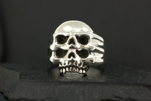 A silver skull-shaped ring with detailed features on a dark background.