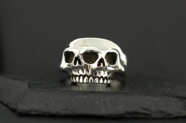 A silver ring featuring three skulls side by side.