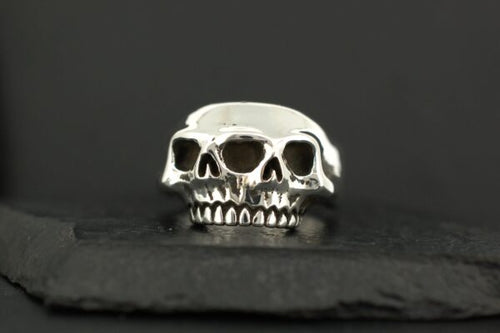 A silver ring featuring three skulls side by side.