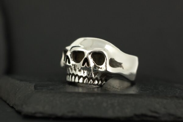 Silver skull-shaped ring on a black surface.