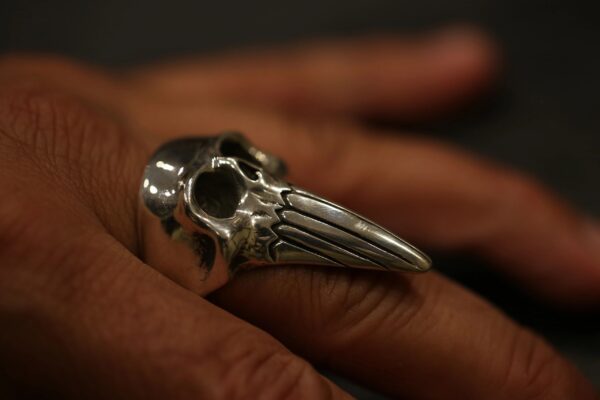 A silver skull ring with elongated teeth worn on a finger.