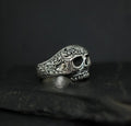 Intricately designed silver skull ring with detailed engravings on a dark background.