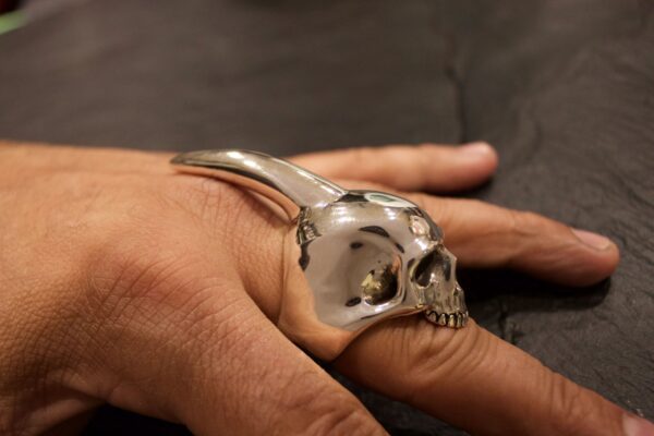 A hand wearing a silver skull-shaped ring with a curved spike.